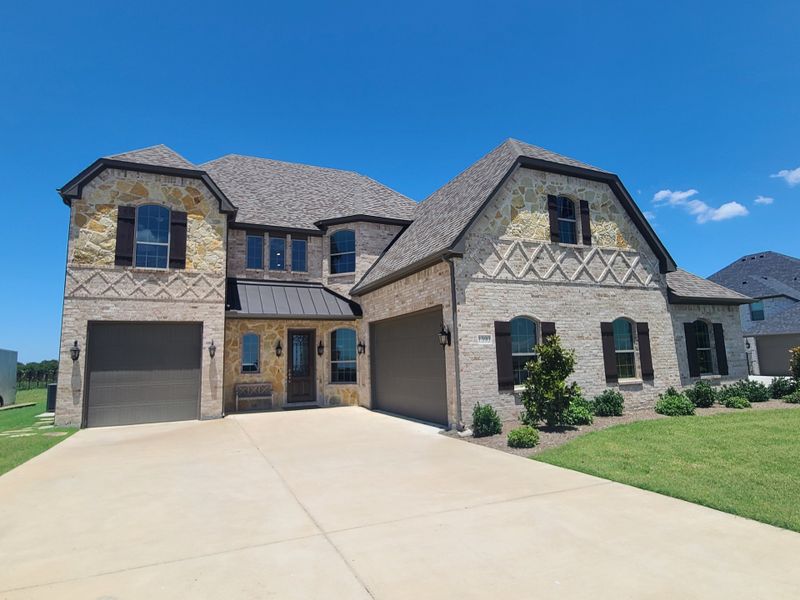 A beautiful stone and brick home with lush landscaping in Corner Stone Ranch by Astoria Homes (Howe, TX).