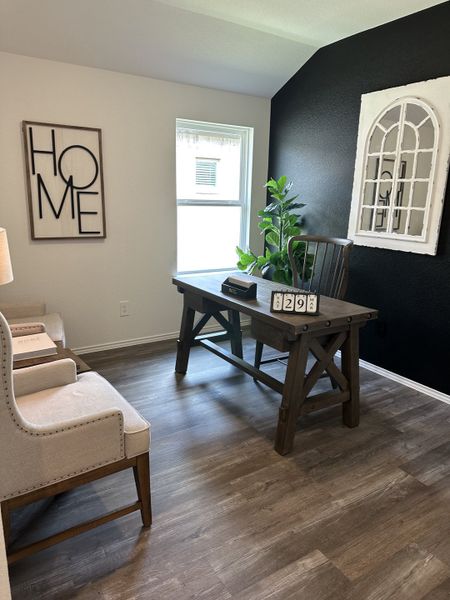A cozy home office featuring a rustic wooden desk, chic armchairs, and a bold accent wall with stylish decor.