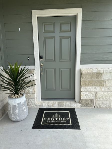 A welcoming entrance with a green door, potted plant, and Century Communities mat in Northpark South by Century Communities (Porter, TX).