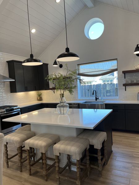 A modern kitchen featuring a vaulted ceiling, island with seating, black cabinetry, and industrial pendant lighting. A modern kitchen featuring a vaulted ceiling, island with seating, black cabinetry, and industrial pendant lighting.