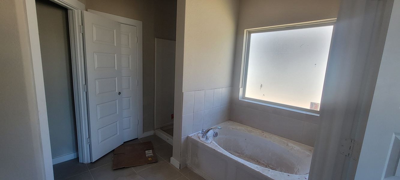 A bathroom featuring a built-in bathtub with frosted window, neutral tiles, and a white paneled door.