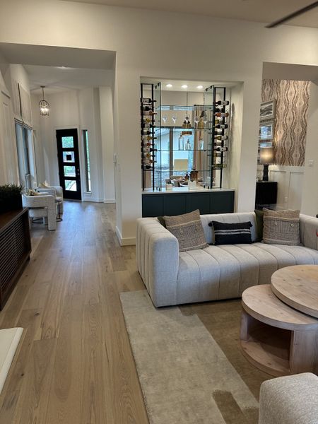 A modern living room with a plush sectional sofa, built-in wine display, and warm wood flooring.