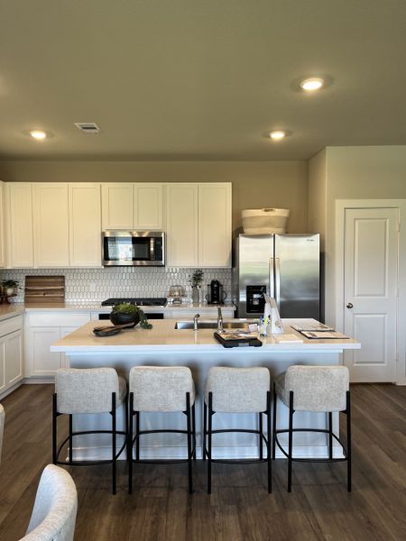 A modern kitchen with white cabinets, a sleek island, and stylish barstools, complemented by elegant lighting.