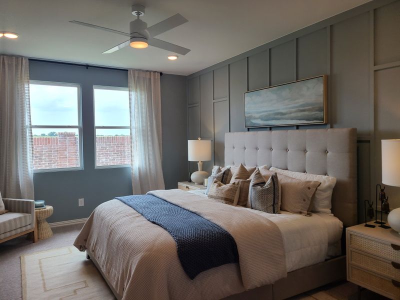 A cozy bedroom with a tufted headboard, patterned pillows, and elegant lighting, featuring a soothing gray accent wall.