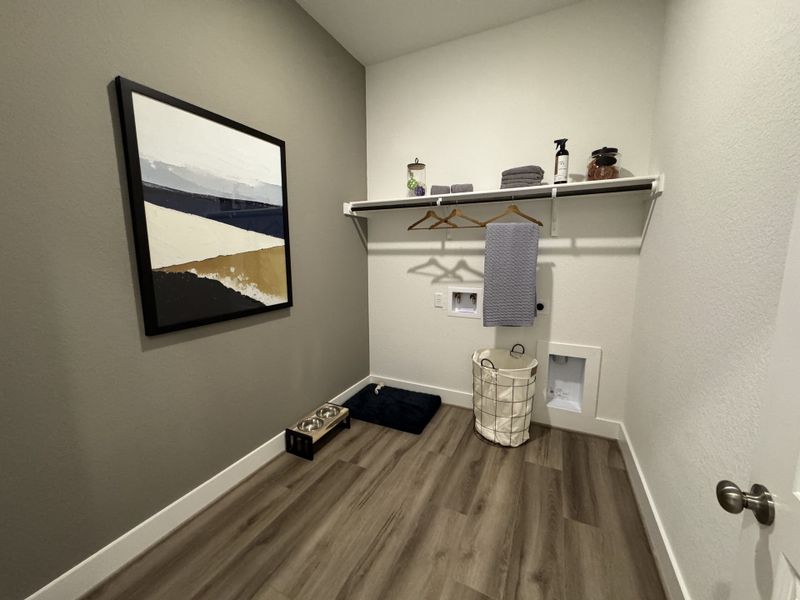 A chic utility room with sleek wooden floors, modern art, and practical shelving with storage baskets and hangers.