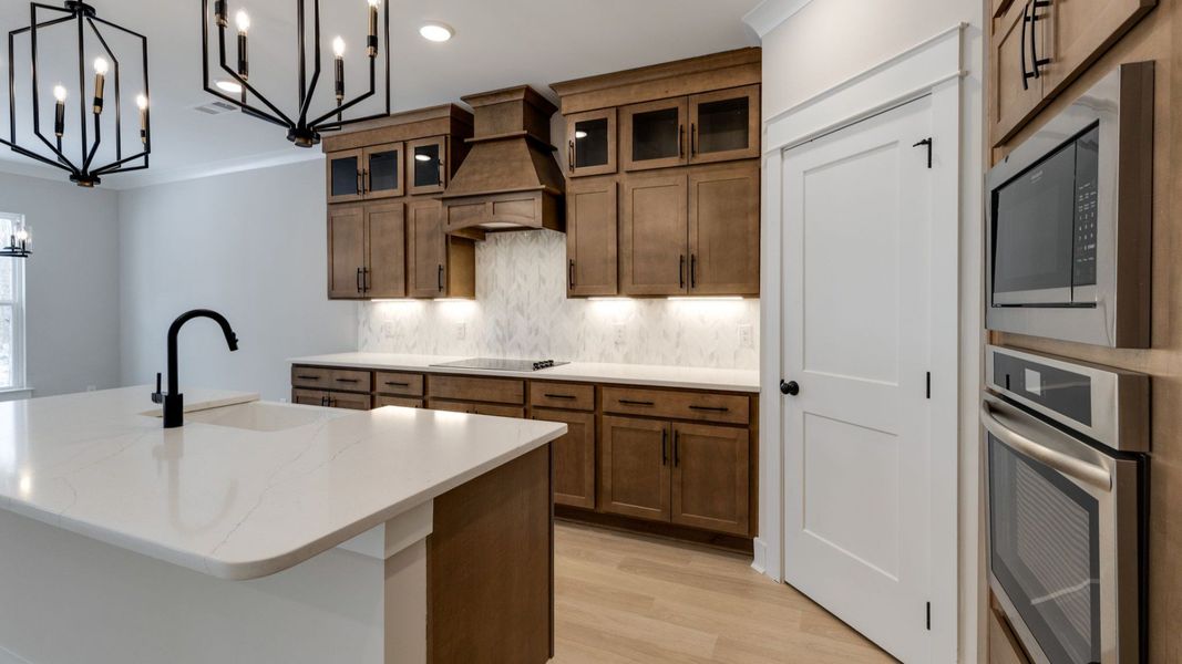 Luxurious kitchen with tasteful dark cabinetry, pendent lighting, tile backsplash, and pantry Luxurious kitchen with tasteful dark cabinetry, pendent lighting, tile backsplash, and pantry