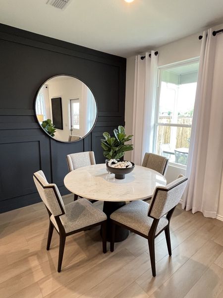 A chic dining area featuring a marble round table, elegant chairs, and a stylish black accent wall with a round mirror. A chic dining area featuring a marble round table, elegant chairs, and a stylish black accent wall with a round mirror.