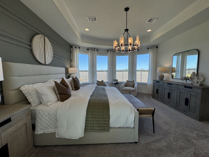 A sophisticated bedroom featuring an elegant chandelier, plush bedding, and ample natural light through large windows.