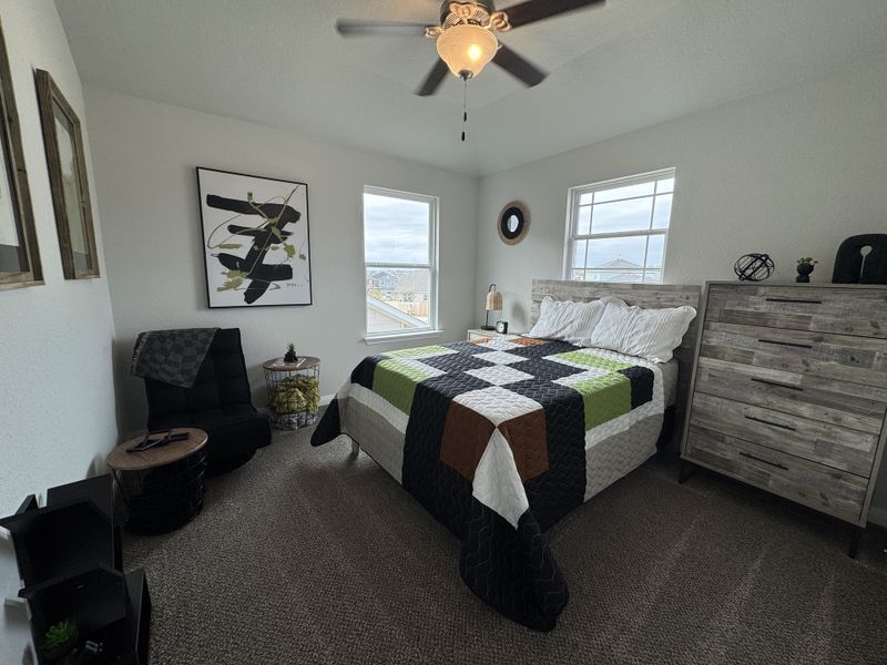 A cozy bedroom with modern artwork, a patchwork quilt, and rustic wood furniture. Ceiling fan enhances comfort.