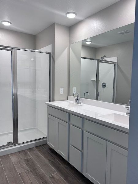 A modern bathroom featuring a sleek glass shower, dual sinks, and elegant wood-style flooring.