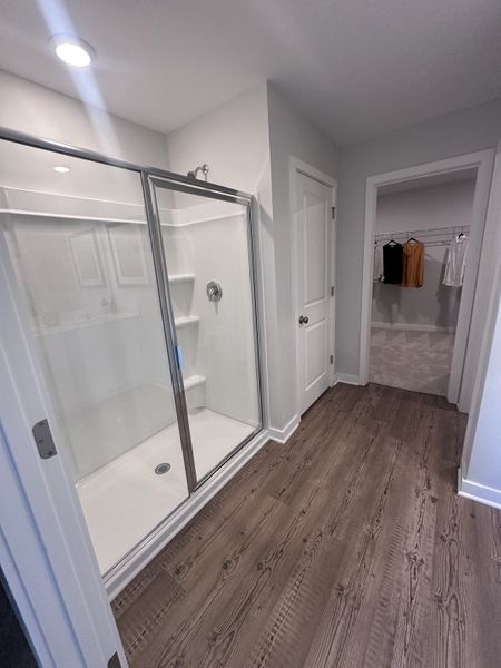 A modern bathroom with a sleek glass shower, wooden flooring, and a spacious walk-in closet.