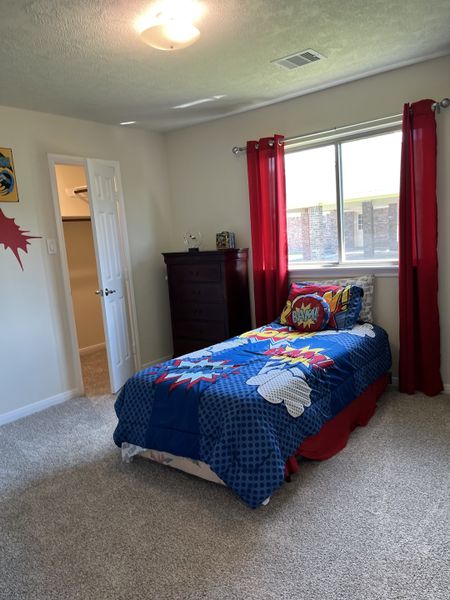 A vibrant child's bedroom featuring colorful bedding, red curtains, and soft carpet flooring.