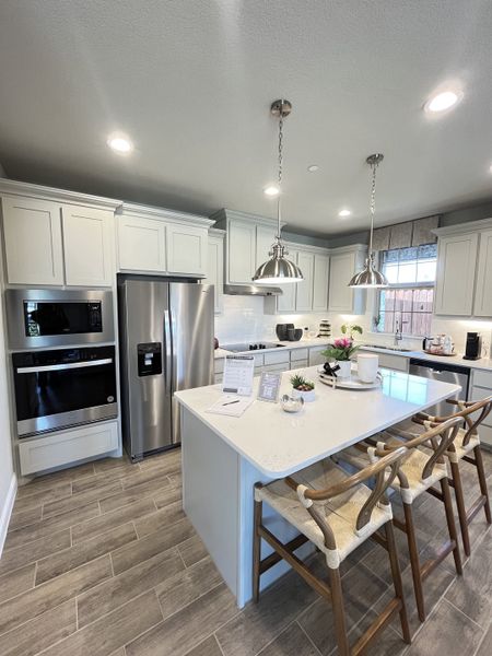 A modern kitchen with a large island, stainless appliances, and elegant pendant lights over wood-tiled floors. A modern kitchen with a large island, stainless appliances, and elegant pendant lights over wood-tiled floors.