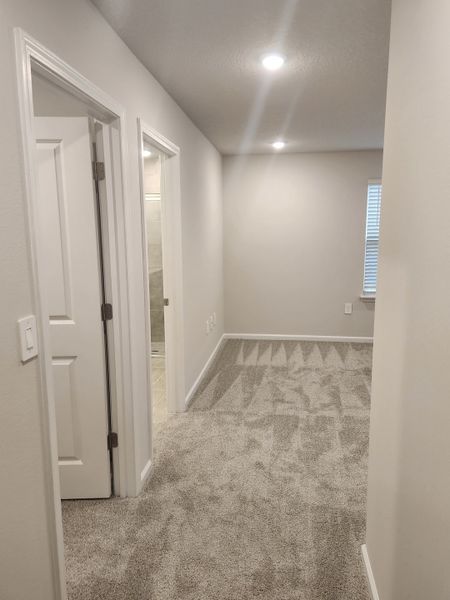 A cozy hallway with soft carpet, neutral walls, and recessed lighting leading to doors on the left. A cozy hallway with soft carpet, neutral walls, and recessed lighting leading to doors on the left.
