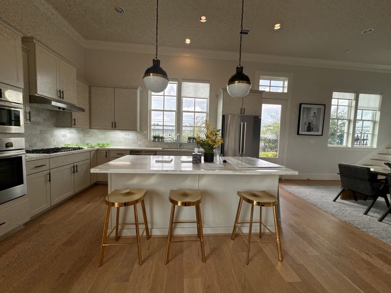 A modern kitchen with a large island, pendant lighting, and sleek cabinetry, opening to a cozy dining area.
