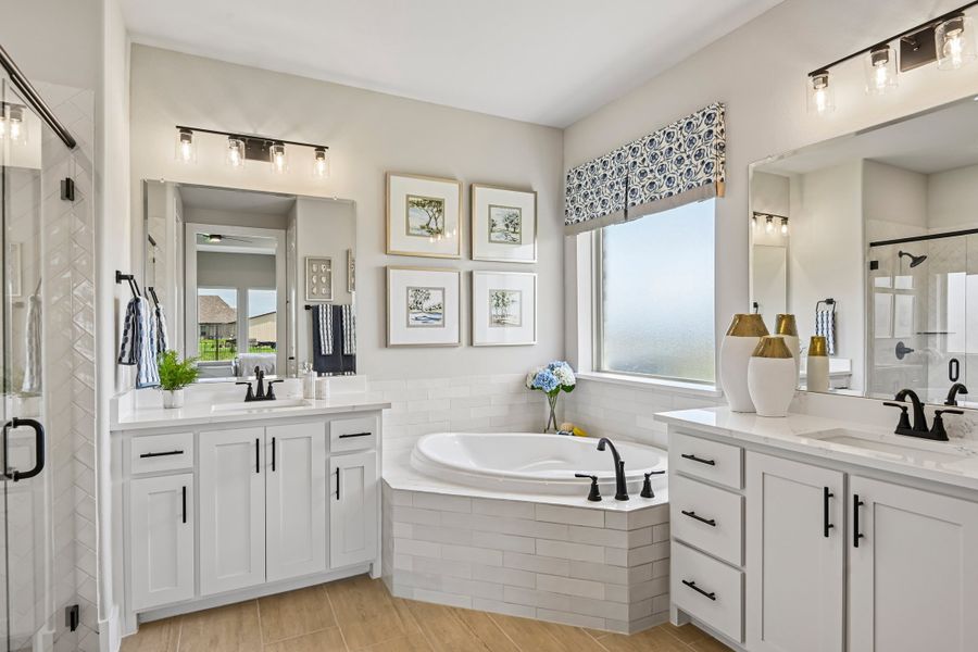 Master bathroom with dual vanities, corner soaking tub, white cabinets, and black fixtures on wood-look tile floors Master bathroom with dual vanities, corner soaking tub, white cabinets, and black fixtures on wood-look tile floors