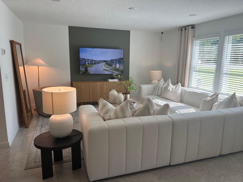 A cozy living room with a plush sectional sofa, large TV, and abundant natural light streaming through the windows.
