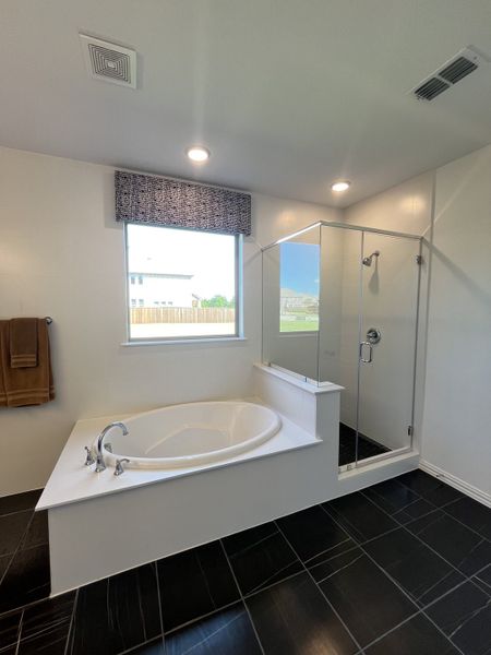 A modern bathroom with a spacious corner bathtub, glass-enclosed shower, and sleek black tile flooring.