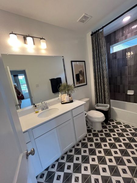 A sleek bathroom with geometric floor tiles, modern lighting, and dark-tiled shower, featuring a white vanity.