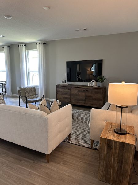 A cozy living room with plush white sofas, modern TV setup, and soft natural lighting through large windows.