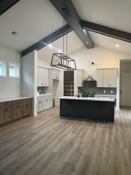 A spacious kitchen with vaulted ceilings, sleek cabinetry, and modern lighting. Features a large island and wood floors. A spacious kitchen with vaulted ceilings, sleek cabinetry, and modern lighting. Features a large island and wood floors.