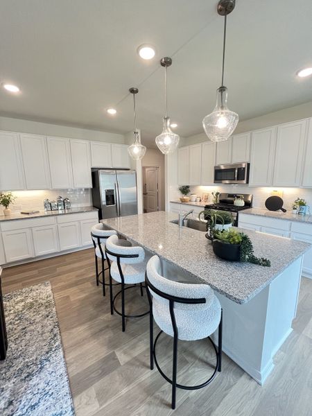 A modern kitchen with sleek white cabinetry, granite countertops, and elegant pendant lighting.
