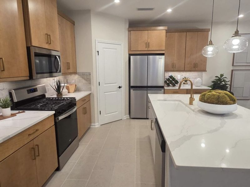 Modern kitchen with sleek stainless appliances, wood cabinets, and a spacious marble island under elegant pendant lighting.