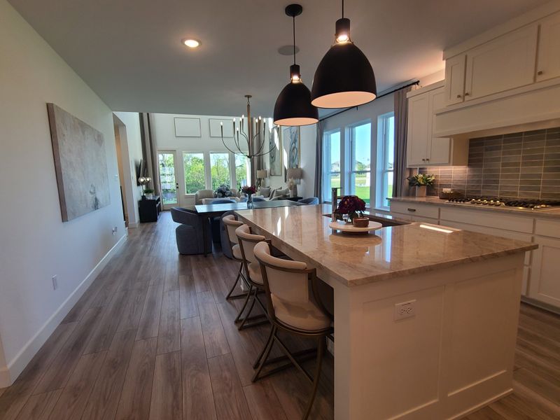 A modern kitchen with a marble island, pendant lights, open layout, and large windows bringing in natural light.