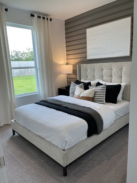 A cozy bedroom with a tufted headboard, striped accent wall, and elegant bedding, featuring soft lighting and large window views.