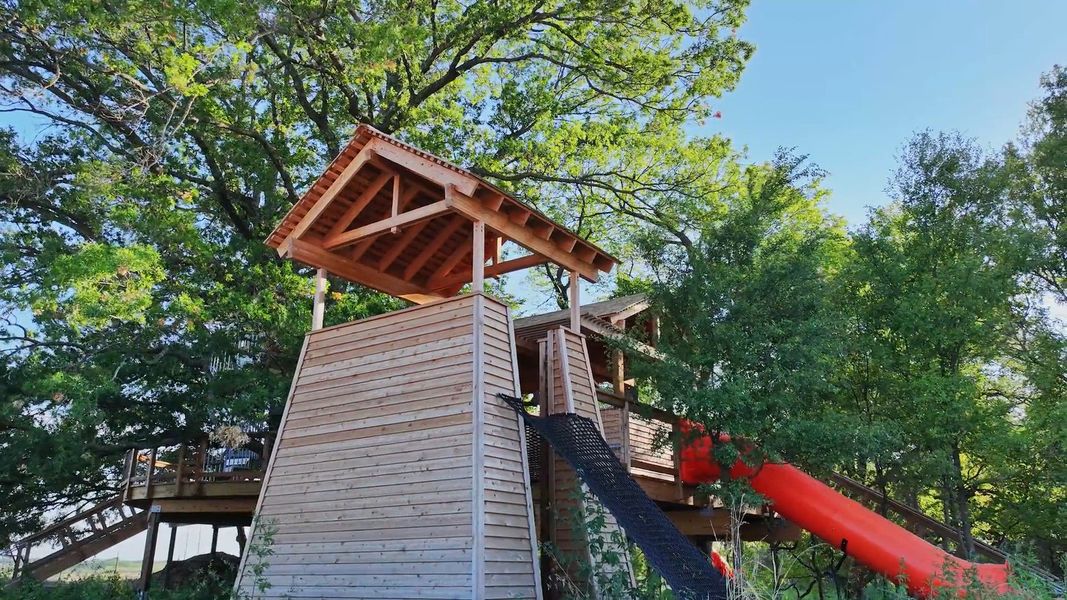 Exceptional wooden treehouse with a vibrant slide offers unparalleled charm amid the trees of Solterra, Texas.