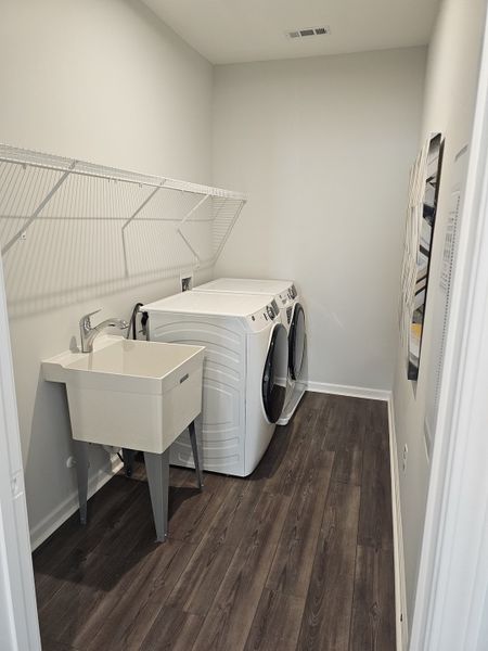 A modern laundry room featuring sleek hardwood floors, washer, dryer, and a utility sink. Perfect for efficient laundering.