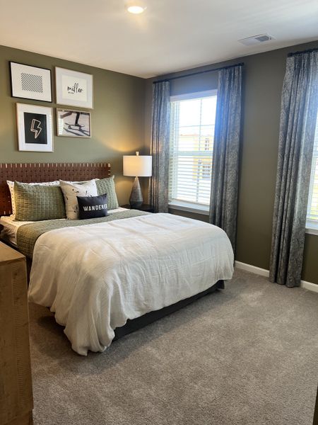 A cozy bedroom featuring green walls, stylish wall art, and large windows with elegant drapery.