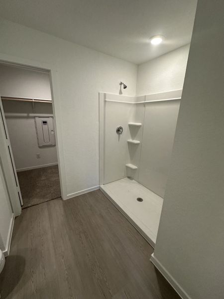 A modern bathroom with a spacious walk-in shower, sleek light fixtures, and wood-inspired flooring.