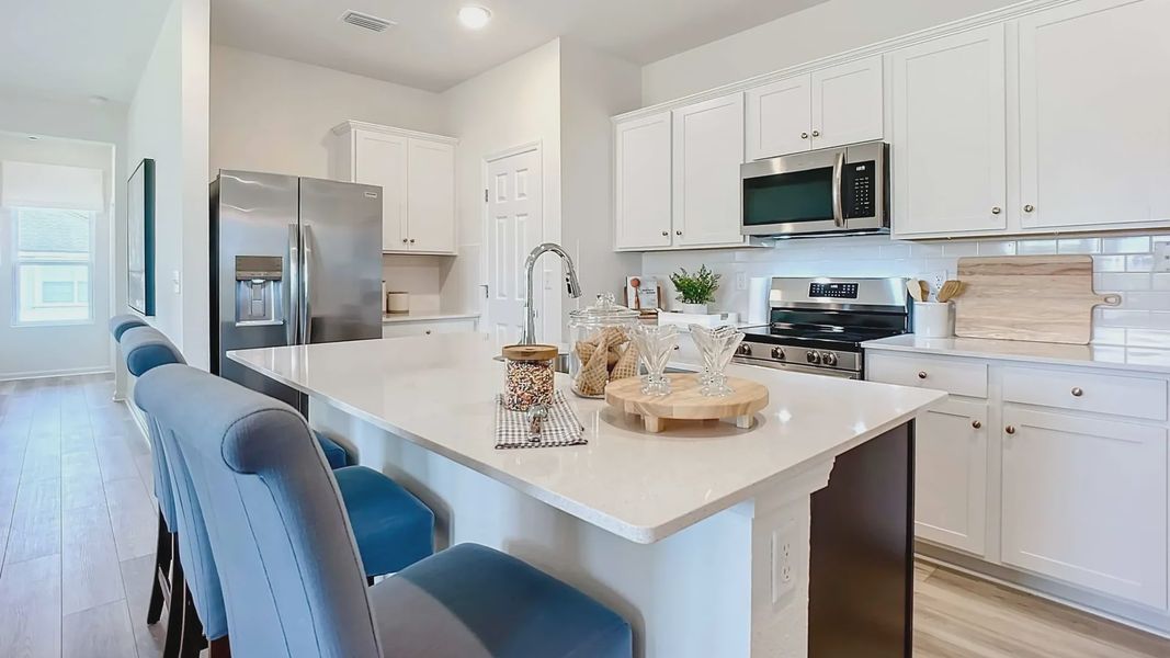 Luxurious kitchen in Panther Creek boasts sleek white cabinetry, marble island, and premium stainless appliances.