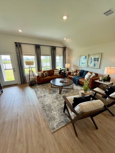 A cozy living room featuring leather sofas, a modern rug, large windows with drapes, and stylish decor accents.