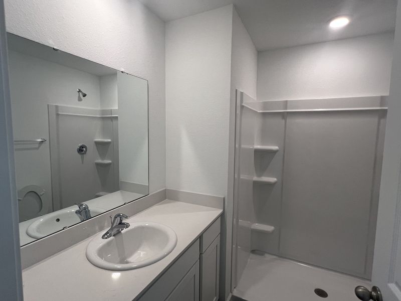 A modern bathroom featuring a sleek shower, large mirror, and a clean, white vanity with integrated sink. A modern bathroom featuring a sleek shower, large mirror, and a clean, white vanity with integrated sink.