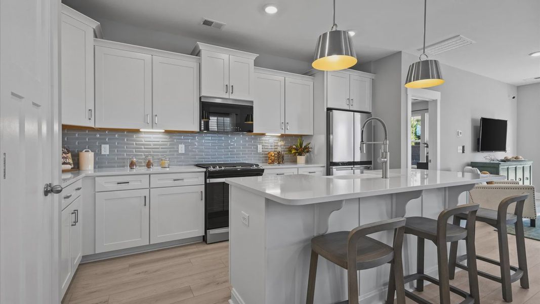 Large kitchen with white cabinetry, gray backsplash, and large island with room for counter stools at Pleasant Falls