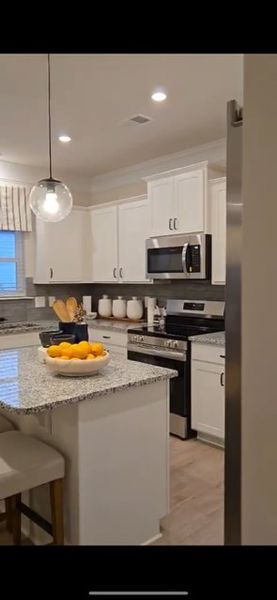 A modern kitchen featuring white cabinetry, granite countertops, and stainless steel appliances with stylish pendant lighting.