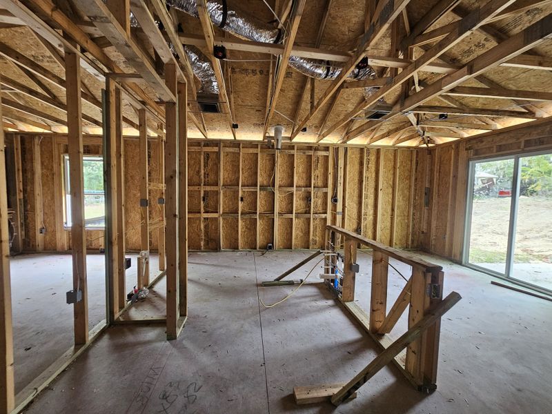 A partially constructed room with exposed wooden framing, ductwork, and a sliding glass door leading outside.