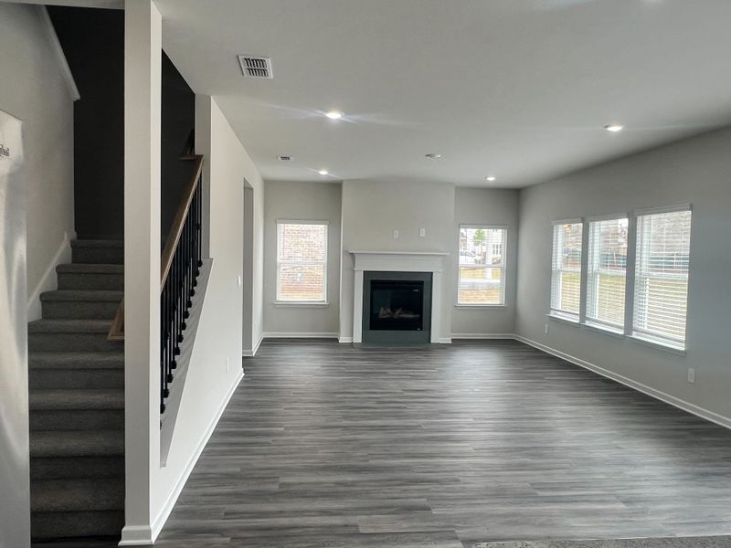 A spacious living room with a modern fireplace, large windows, and sleek gray flooring, leading to a carpeted staircase. A spacious living room with a modern fireplace, large windows, and sleek gray flooring, leading to a carpeted staircase.