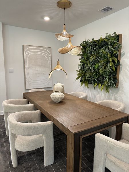 A modern dining area with a wooden table, plush chairs, pendant lighting, and a vertical garden accenting the wall. A modern dining area with a wooden table, plush chairs, pendant lighting, and a vertical garden accenting the wall.
