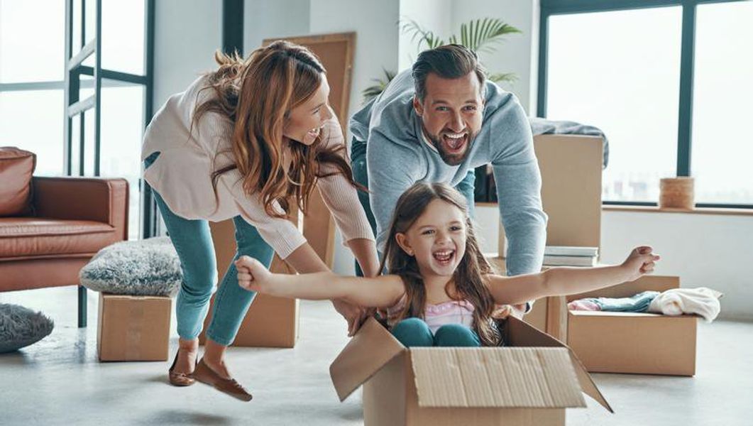 Stock photo of a cheerful young family smiling and unboxing their stuff while moving into a new home.