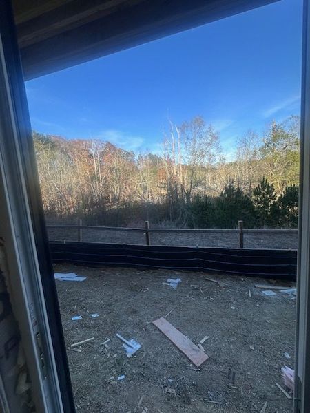 A scenic backyard view with a rustic fence surrounded by trees and a clear blue sky.