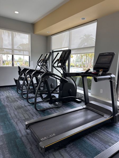 A modern gym with state-of-the-art treadmills and ellipticals, surrounded by large windows for natural light. A modern gym with state-of-the-art treadmills and ellipticals, surrounded by large windows for natural light.