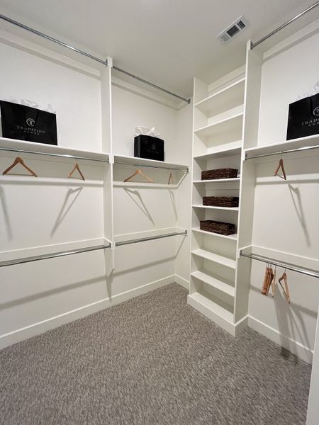 A spacious walk-in closet with ample shelving, hanging rods, and a cozy carpet floor.