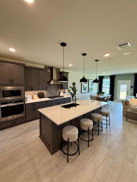 A modern kitchen with a sleek island, cozy seating, pendant lighting, and stainless steel appliances.