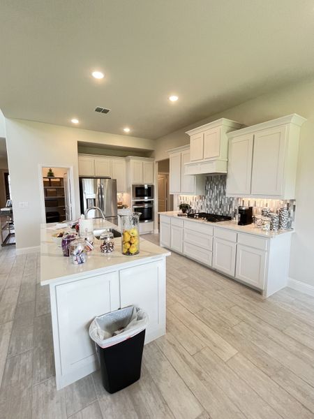 A modern kitchen featuring sleek white cabinetry, stainless steel appliances, and a spacious island with elegant lighting.