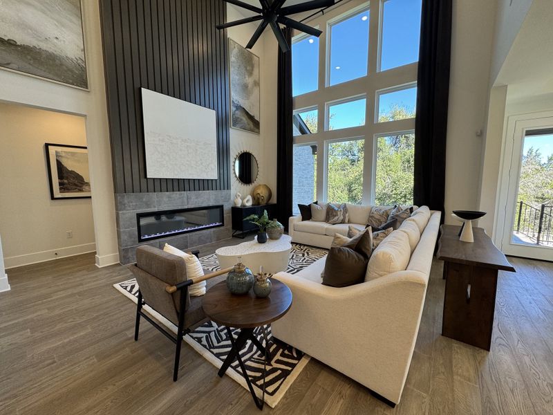 A sophisticated living room with a high ceiling, large windows, chic fireplace, and elegant furnishings.