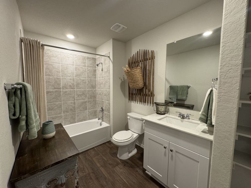A cozy bathroom with a tiled bathtub, dark wood accents, and bright lighting, featuring stylish decor and modern amenities.