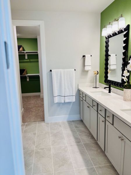 A modern bathroom with a striking green accent wall, elegant tile flooring, and a spacious vanity with dual sinks.
